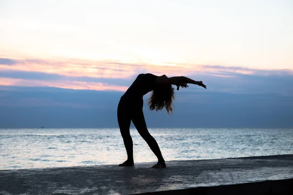 unrecognizable senoir woman with beautiful body doing yoga at sunrise on the sea, silhouette of yoga poses