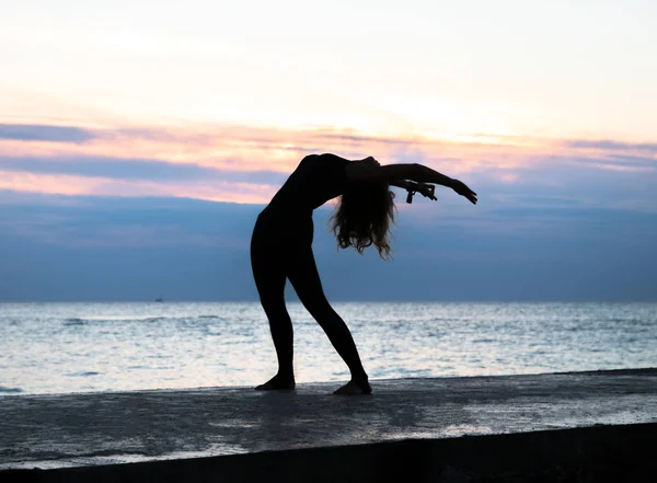 Felismerhetetlen szenoir nő gyönyörű szervezet csinál jóga napkelte a tengeren, a jóga sziluettje jelent — Stock Fotó