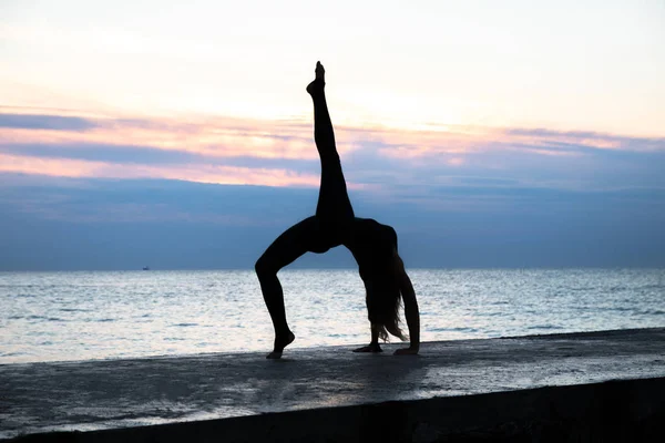 Неузнаваемая сенуар-женщина с красивым телом, профессионально занимающаяся йогой на восходе солнца на море, силуэт поз йоги — стоковое фото