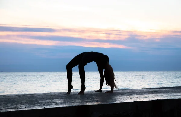 Felismerhetetlen Senoir nő gyönyörű szervezet profissiionally csinál jóga a napfelkeltét a tengeren, sziluettje jóga pózok — Stock Fotó