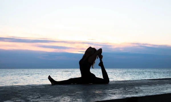 Onherkenbaar Ernest vrouw met mooi lichaam doet yoga splitst bij zonsopgang op de zee, silhouet van yoga poses — Stockfoto