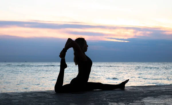 Mulher senoir irreconhecível com belo corpo fazendo divisões de ioga ao nascer do sol no mar, silhueta de poses de ioga — Fotografia de Stock