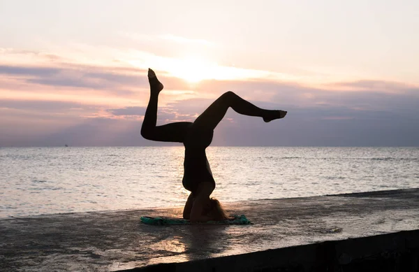 Nierozpoznawalna kobieta z pięknym ciałem robi głowę jogi na wschód słońca na morzu, sylwetka jogi stwarza — Zdjęcie stockowe