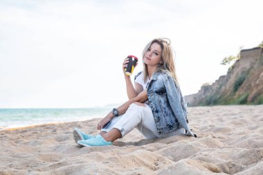 Genç ve çekici bir kadın kumsalda dinleniyor. Kahvesini yudumluyor.