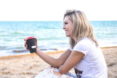 Genç, çekici, sarışın, kahve fincanı olan kadın denize bakıyor.