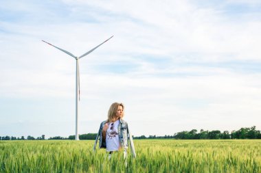 Rüzgâr türbini jeneratörlerinin yanındaki buğday tarlasında genç ve çekici bir kadın. Gün batımı turuncu ışığı.