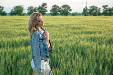Genç ve çekici bir kadın buğday tarlasında rüzgâr türbini jeneratörlerinin yanında, gün batımında.