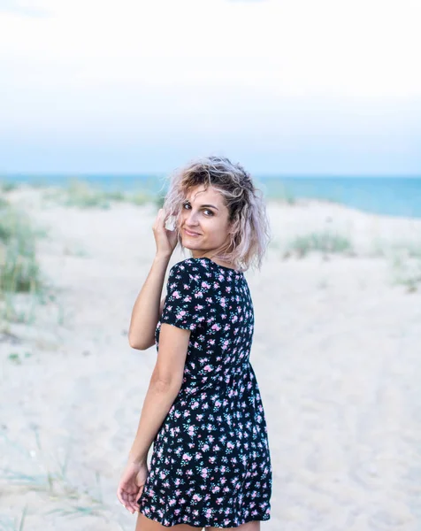 Tanned beautiful young woman in cute dresswith flowers on the beach in clouds weather — Stock Photo, Image