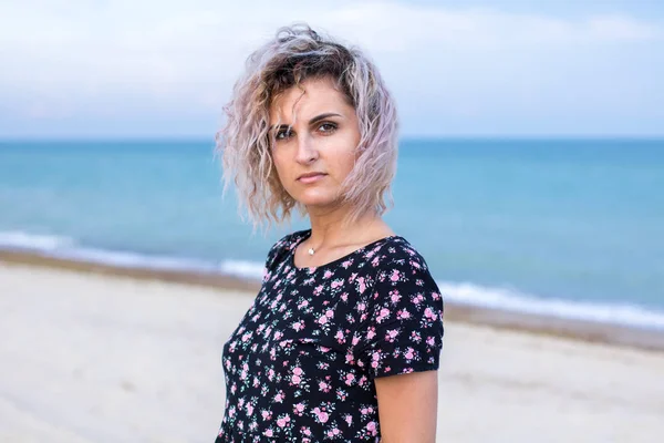 Bronceada hermosa mujer joven en lindo dresswith flores en la playa en las nubes tiempo —  Fotos de Stock