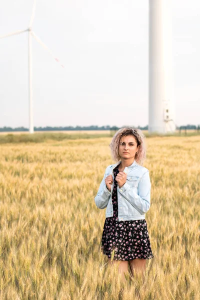 Kotlu ceketli, buğday tarlasında giyinmiş, günbatımında bronzlaşmış kıvırcık saçlı genç bir kadın.