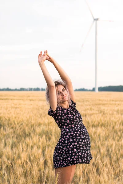 Genç, bronzlaşmış, kıvırcık saçlı kadın gün batımında olgunlaşmış buğday tarlasında olmaktan mutlu.