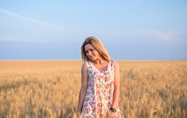 Günbatımında sarı buğday tarlasında giyinmiş genç, baştan çıkarıcı, kırsal sarı saçlı kadın.