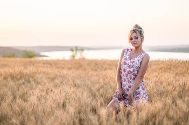 Günbatımında sarı buğday tarlasında, arka planda gölde, sarı saçlı, baştan çıkarıcı genç, kırsal saçlı kadın.