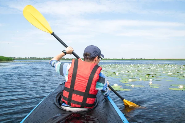 Hombre con remo en kayak en el lago, nenúfares alrededor — Foto de Stock