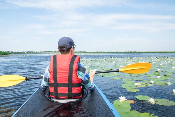 Mann mit Paddel im Kajak auf dem See, Seerosen herum — Stockfoto