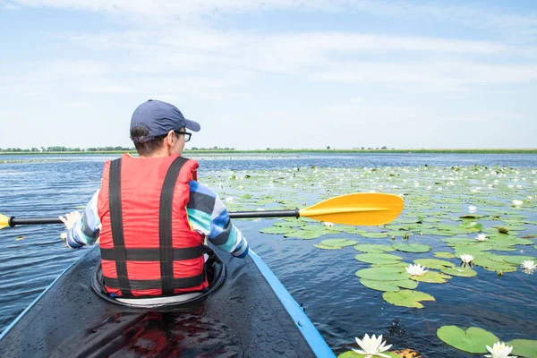 Mann mit Paddel im Kajak auf dem See, Seerosen herum — Stockfoto