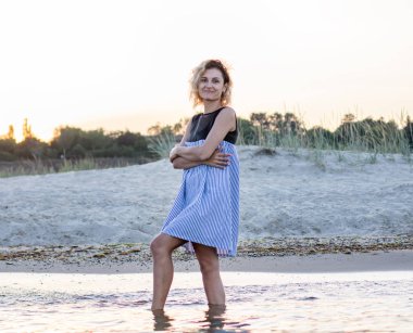 elbise kıvırcık kılları ile kadın sahilde suda duruyor, arka planda gün batımı