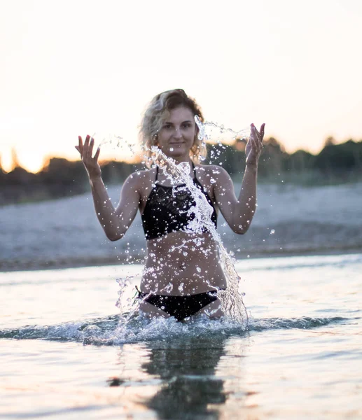 Fille aux cheveux bouclés en maillot de bain noir debout dans l'eau de mer et l'eau de source, coucher de soleil sur le fond — Photo