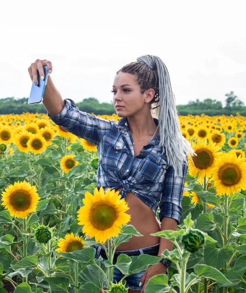 young cute tanned country girl with afro-braids on the sunflowers field making selfie