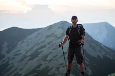 sırt çantası ve trekking çubukları ile kafkas adam yürüyüşçü yeşil taşların zirvesinde dağ gün batımı ışığında dağların panoramik bir görünüm keyfini çıkarın