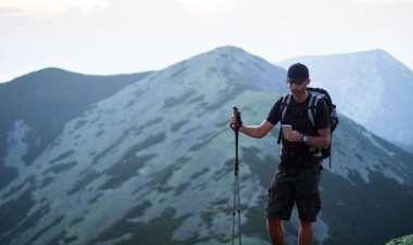 sırt çantası ve trekking çubukları ile kafkas adam yürüyüşçü yeşil taşların zirvesinde dağ akıllı telefon bir şey arıyor