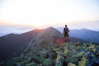 sırt çantası ve trekking çubukları ile kafkas adam yürüyüşçü yeşil taşların zirvesinde dağ gün batımı ışığında dağların panoramik bir görünüm keyfini çıkarın