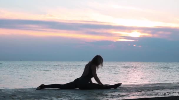 海の日の出でヨガスプリットをする美しいボディを持つ成熟した女性 ヨガポーズのシルエット — ストック動画