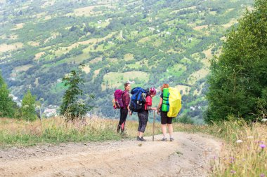 dağ yolu üzerinde üç genç kadın yürüyüşçüler, arka planda tepe