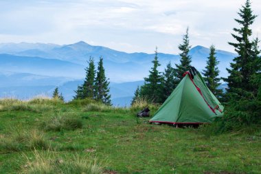 yeşil çadır ve dağlarda glade üzerinde trekking ayakkabı, arka planda sis ile kaplı dağ sırası