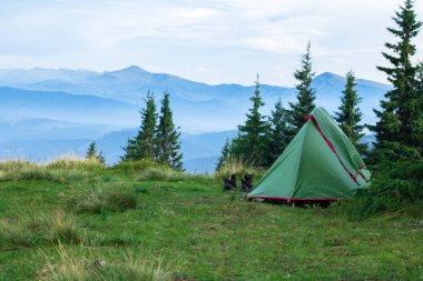 yeşil çadır ve dağlarda glade üzerinde trekking ayakkabı, arka planda sis ile kaplı dağ sırası