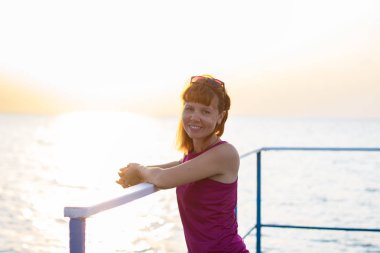 Kızıl saçlı kız gün batımına karşı rıhtımdaki korkulukların yanında