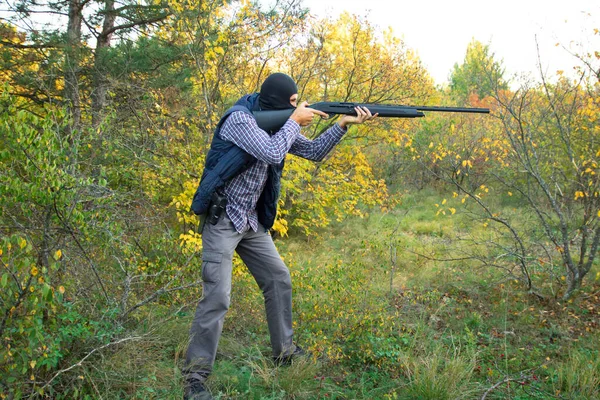 Macho en máscara negra con escopeta semiautomática y pistola en el bosque otoñal apuntando — Foto de Stock