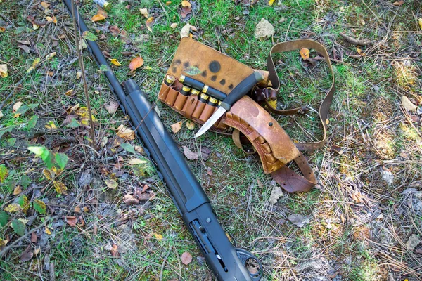Shotgun, cartridge belt, cartridges and knife on grass and ground background — Stock Photo, Image