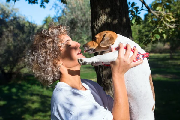 Blondynka kręcone dziewczyna trzyma na ręce i całuje jej zwierzak, Jack Russell pies w jesiennym parku — Zdjęcie stockowe