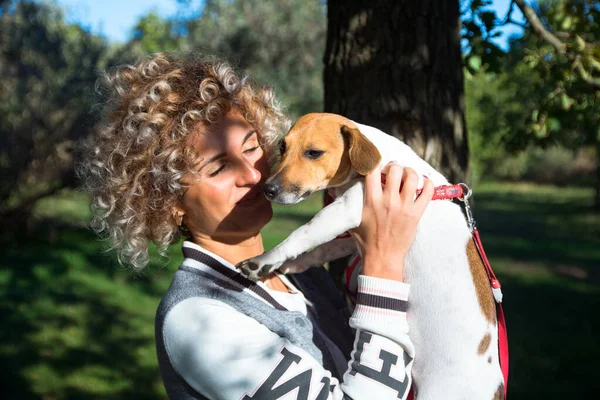 Piękna blondynka kręcone dziewczyna bawi się ze swoim zwierzakiem, Jack Russell pies w zielonym parku jesień — Zdjęcie stockowe