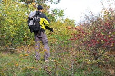Yarı otomatik tüfekli ve sırt çantalı bir adam sonbahar ormanında avlanıyor.