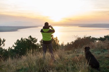 Labrador köpeğiyle gölün üzerinde turuncu gündoğumuna hayran olan bir adam.