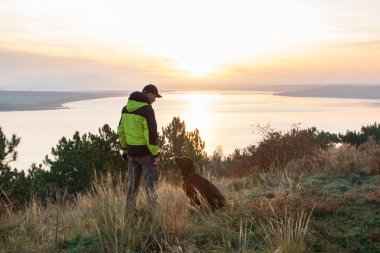 Labrador köpeğiyle gölün üzerinde turuncu gündoğumuna hayran olan bir adam.