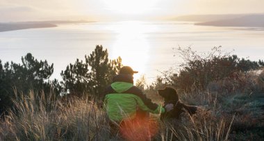 Labrador köpeğiyle gölün üzerinde turuncu gündoğumuna hayran olan bir adam.