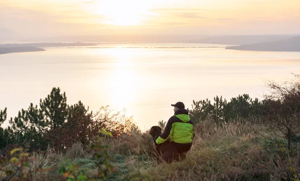 Man with his labrador dog admiring orange sunrise over the lake — ストック写真