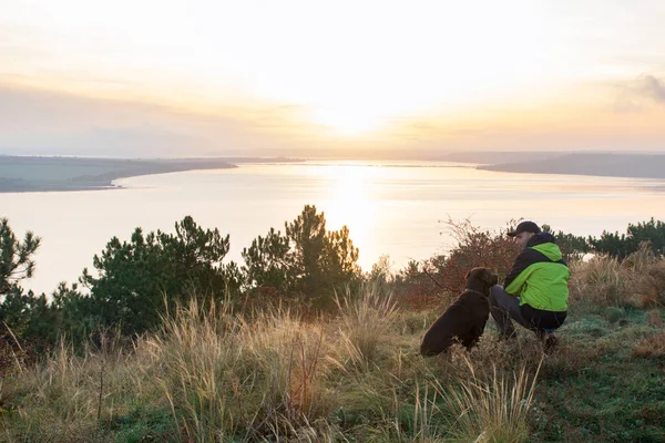 Man with his labrador dog admiring orange sunrise over the lake — ストック写真