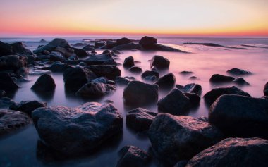 Kırmızı günbatımında pürüzsüz deniz suyundaki taşlar