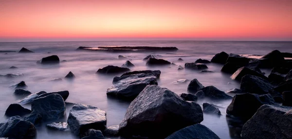 Kırmızı günbatımında pürüzsüz deniz suyundaki taşlar