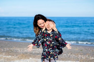 Genç bir kadın ellerini kapadı, küçük kız. Sahilde. Benzer elbiseler