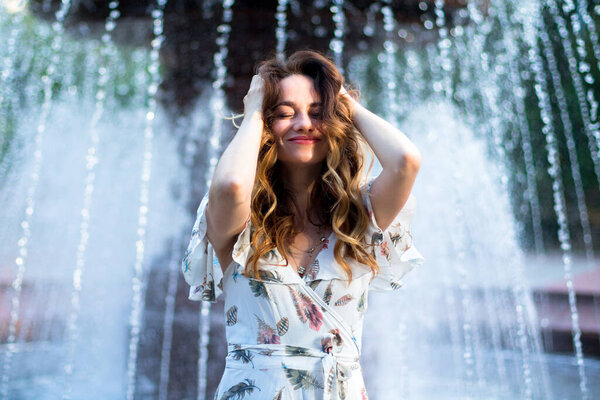 caucasian girl in white dress with flowers feels happy near big fountain on the background