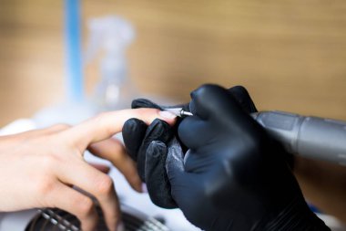 Siyah eldivenli manikürcü manikür matkabıyla manikür yapıyor.