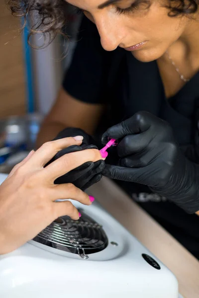 manicurist master in black gloves painting nails in purple in the nail salon