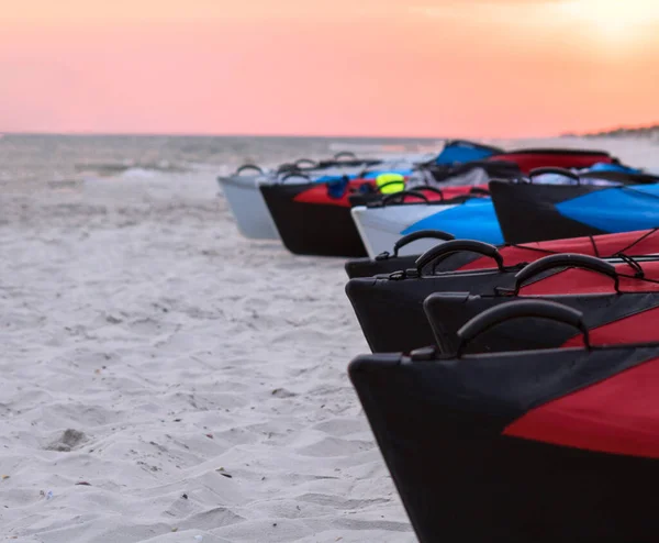 Farklı renkte şişirilebilir kanolar gün batımında vahşi sahilde sıralanır.