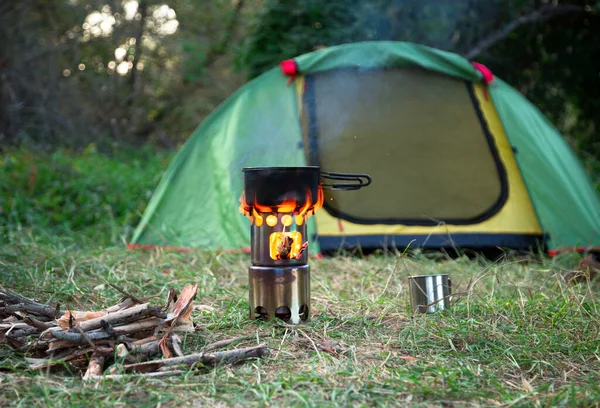 食物是在野营的柴炉上烹调的 后面草地上的绿色帐篷 靠近柴炉的篝火和钢杯 — 图库照片