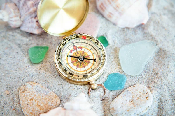 golden compass on the sand among the shells, little stones and colored pieces of glass